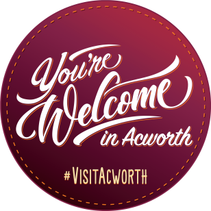 Circular burgundy badge with “You’re Welcome in Acworth” in stylized white text and “#VisitAcworth” below. Circular burgundy badge with "You're Welcome in Acworth" in stylized white text and "#VisitAcworth" below.