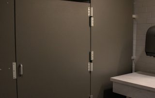 A dimly lit public restroom with green walls, a stall door, gray floor tiles, and a square white sink on the right side.