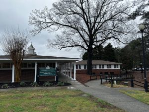 A building with a sign reading "Acorn's Beach House." It has a pathway leading to the entrance, a large tree nearby, and another building in the background. The sky is overcast.