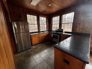 A kitchen with wooden cabinets, black granite countertops, stainless steel appliances including a refrigerator and stove, and large windows providing natural light.