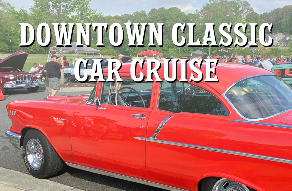 A red vintage car is on display at the Downtown Classic Car Cruise event. Other classic cars and people in the background.