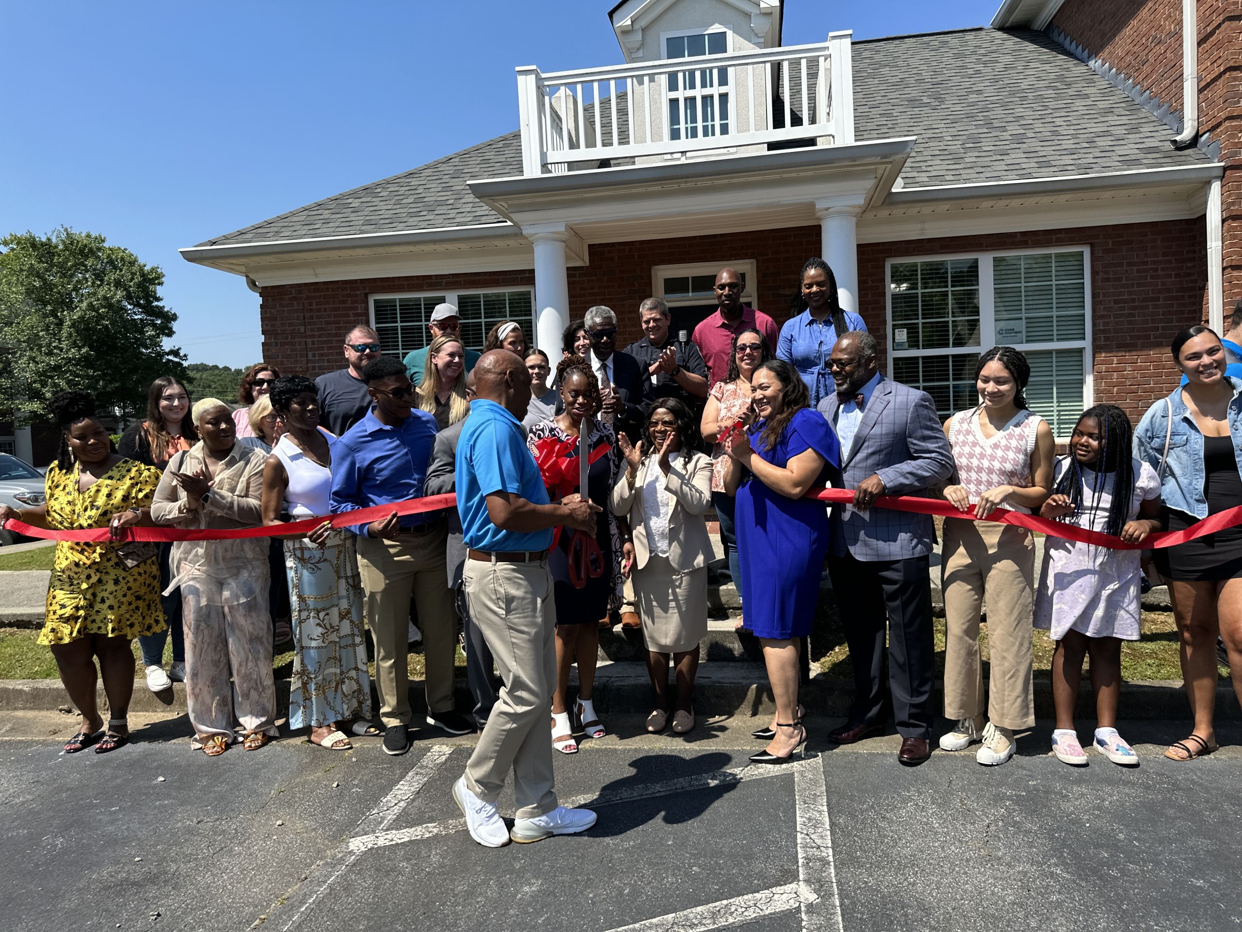 A group of people gathered in front of a building with a red ribbon, about to cut it for a ribbon-cutting ceremony. Northwest Pediatric Care Ribbon Cutting with Alderman Houston.