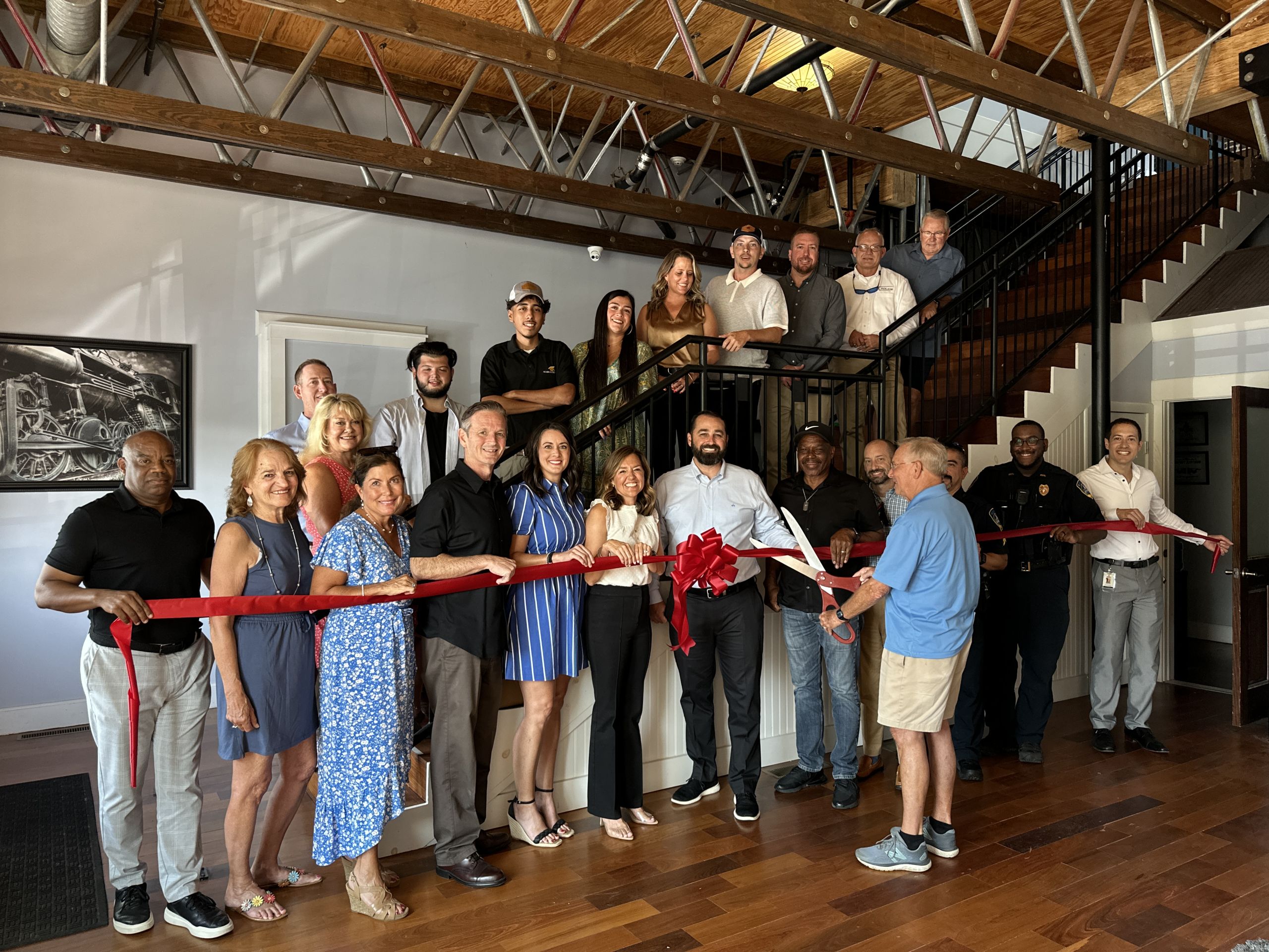 Image Academy Roofing Ribbon Cutting with people holding ribbon and standing in front of and along an indoor staircase.