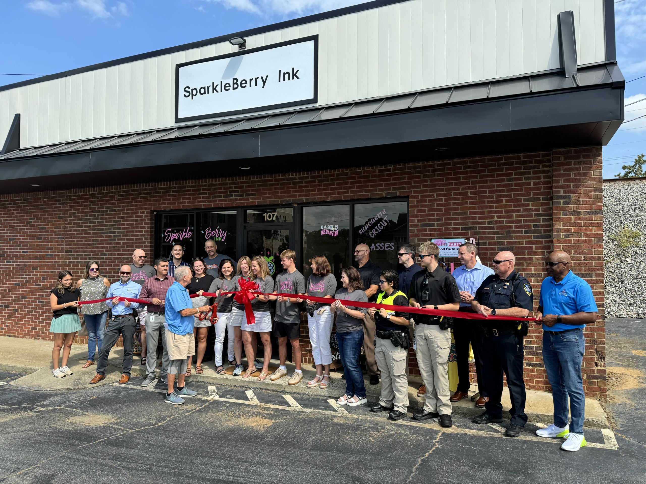 Image a group of people holding a red ribbon outside of Sparkleberry Ink in Acworth