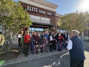 A group of people stand in front of Elite Nail Spa, holding a ribbon and scissors as if for a grand opening event. Balloons are visible in the background.