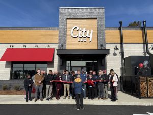 A group of people gathered in front of a City BBQ restaurant for a ribbon-cutting ceremony.