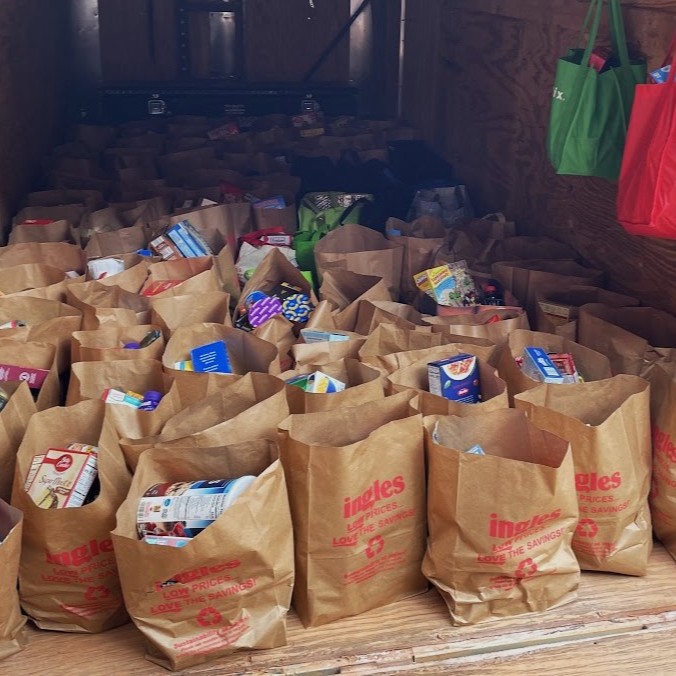Dozens of brown paper grocery bags filled with food items are arranged inside a trailer or storage area. Dozens of brown paper grocery bags filled with food items are arranged inside a trailer or storage area.