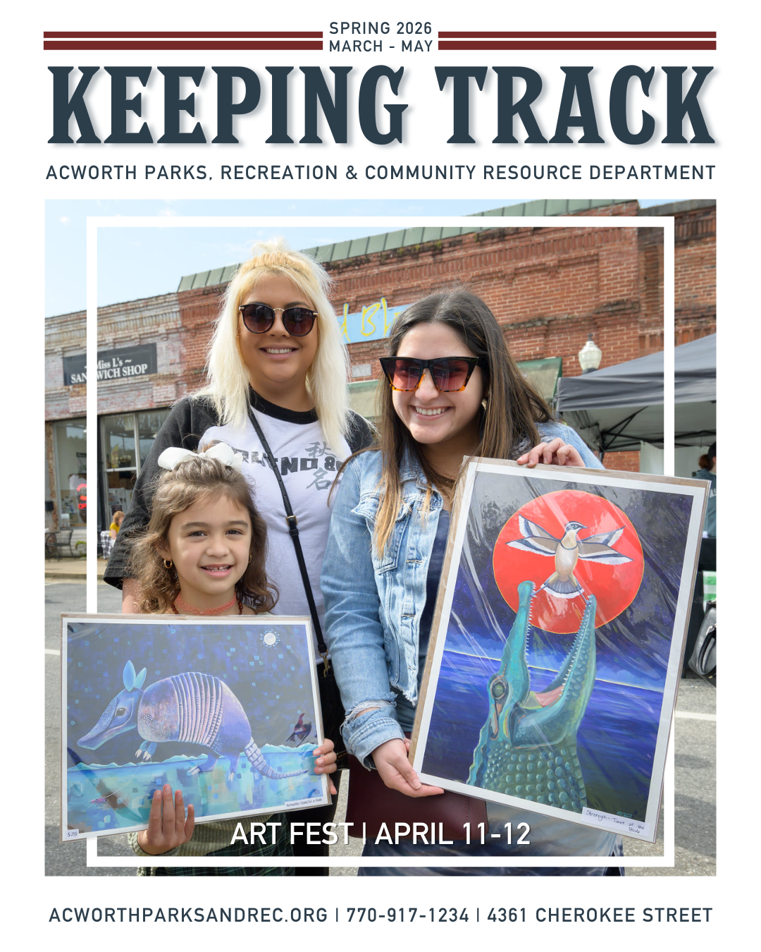 Three people smile outdoors while holding colorful animal-themed artwork at Acworth Art Fest, celebrating local art and recreation. Storefronts and other event-goers are visible in the background.