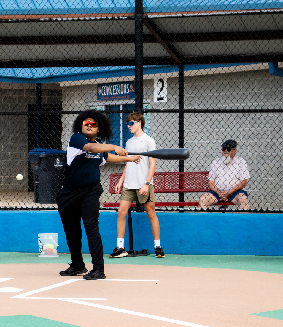 IMG_5237 A person stands at home plate holding a baseball bat, preparing to hit, while three others watch from behind the fence—capturing a classic moment perfect for a Horizon Blog feature.