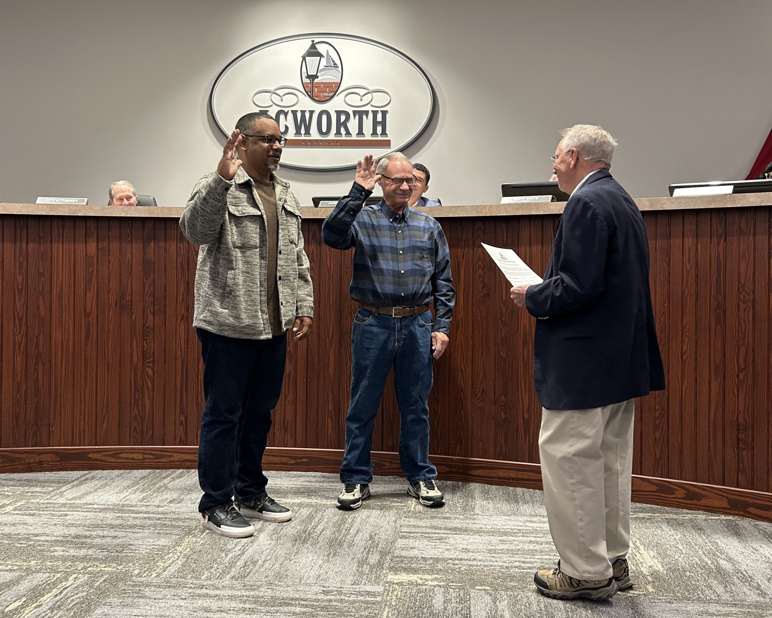 Two men stand with raised right hands, being sworn in as Planning and Zoning Commission Members by an official holding a paper in a council chamber with a "Ringworth" sign in the background.