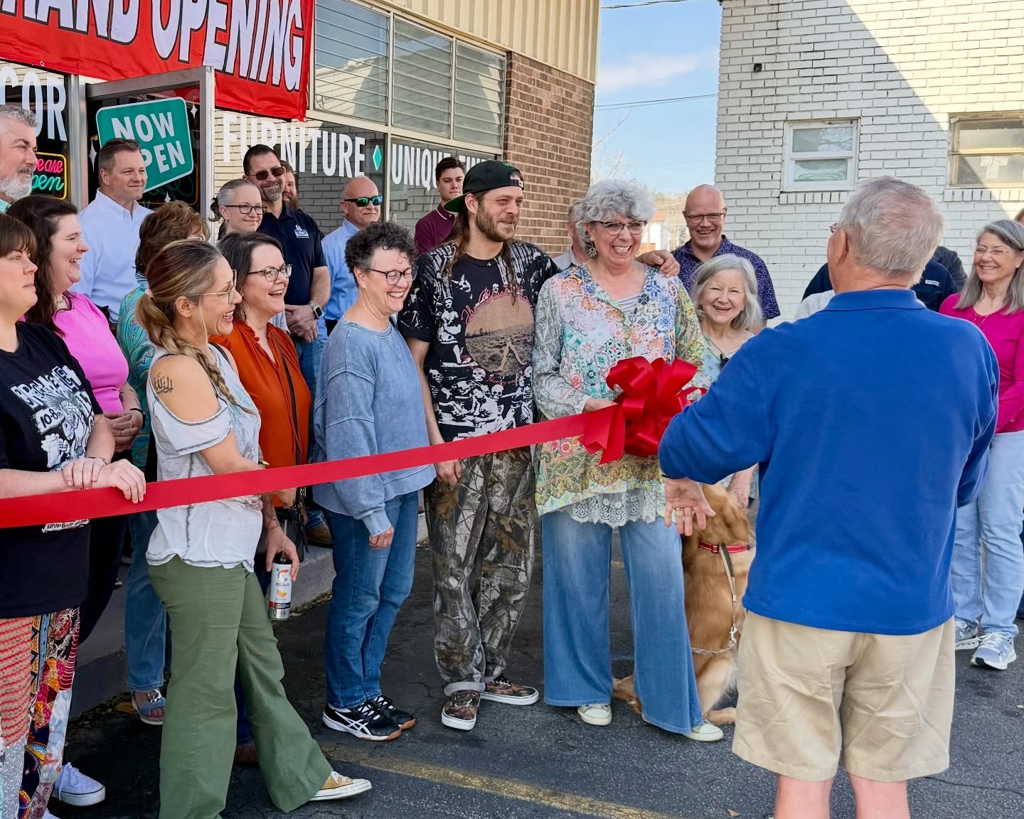 A group of people stand outside Acworth Antiques as a man in a blue shirt prepares for the ribbon cutting, marking a grand opening celebration.