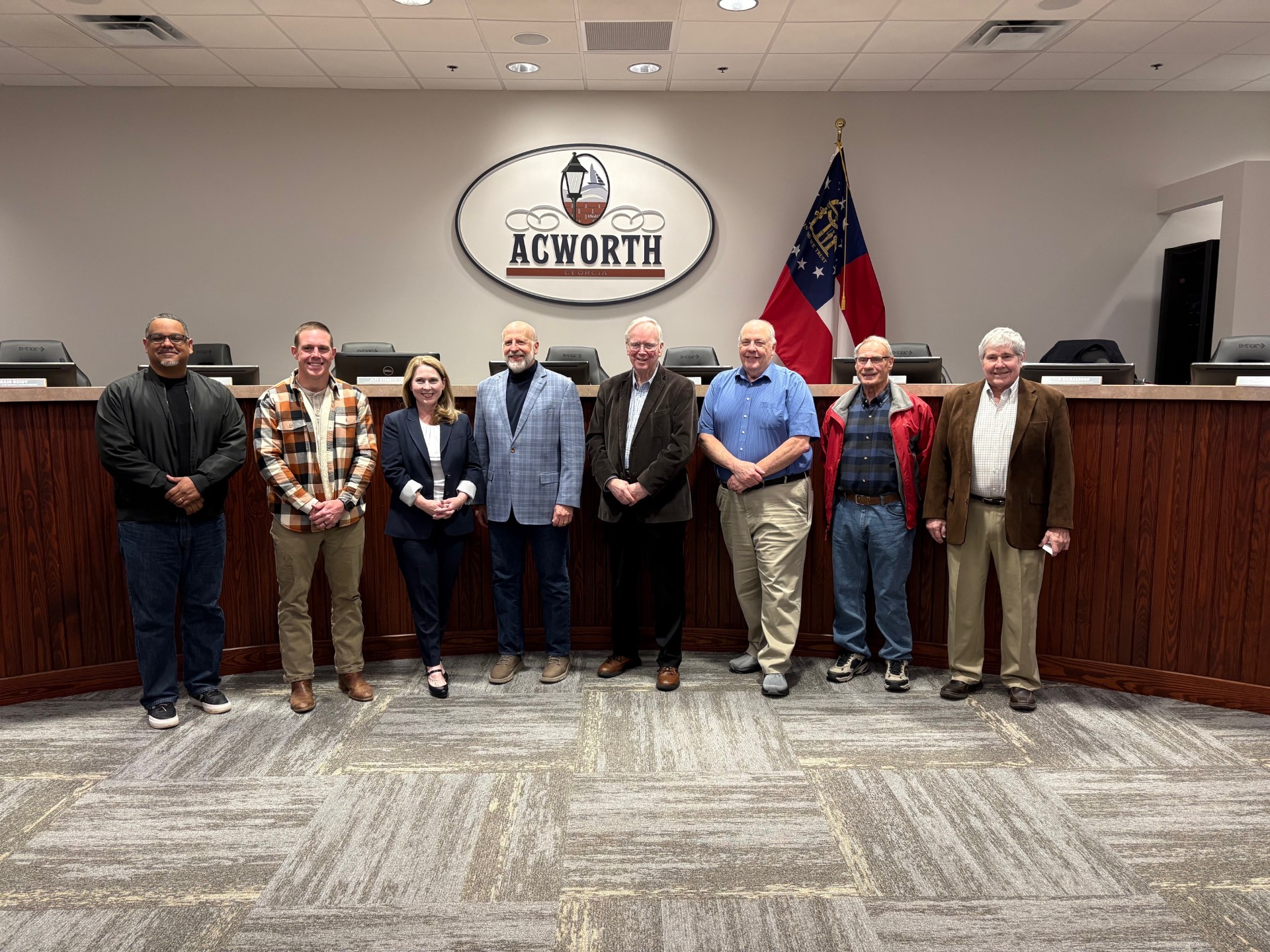 A group of eight people stands in a row inside a government meeting room in front of an